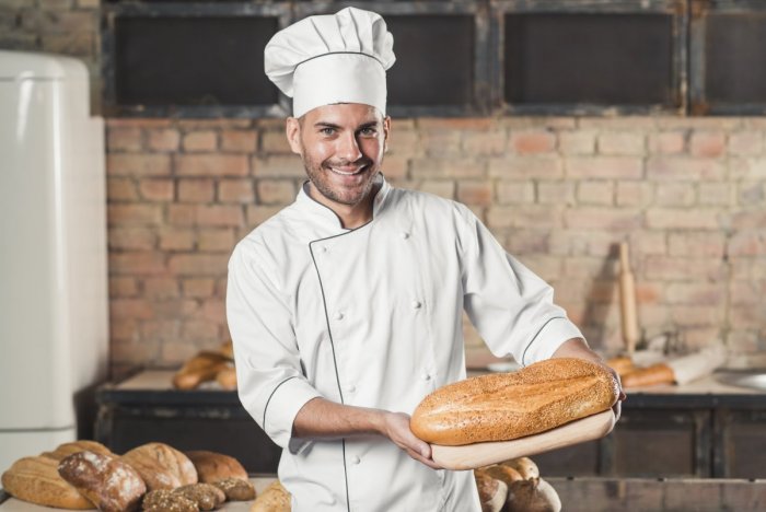 smiling-male-baker-holding-baked-bread-chopping-board.jpg